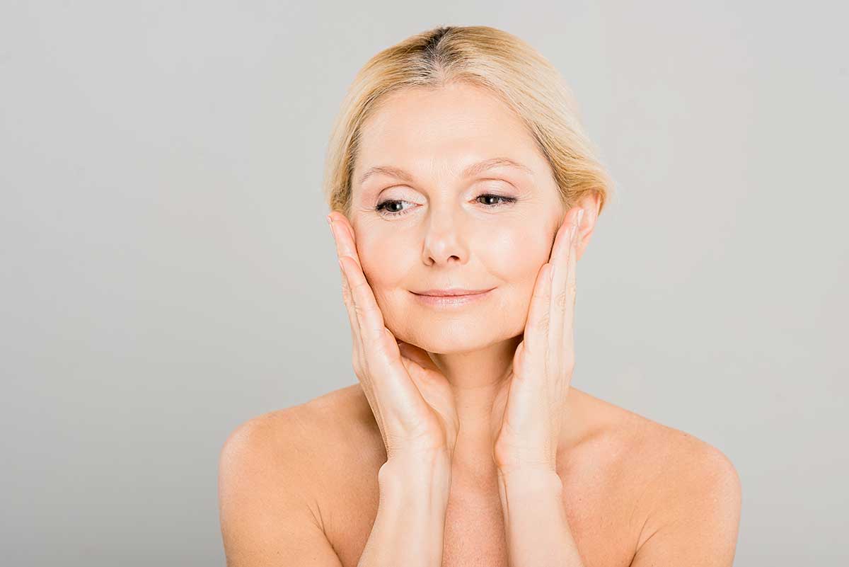 Mature woman touching her face while considering skin changes associated with perimenopause and collagen loss